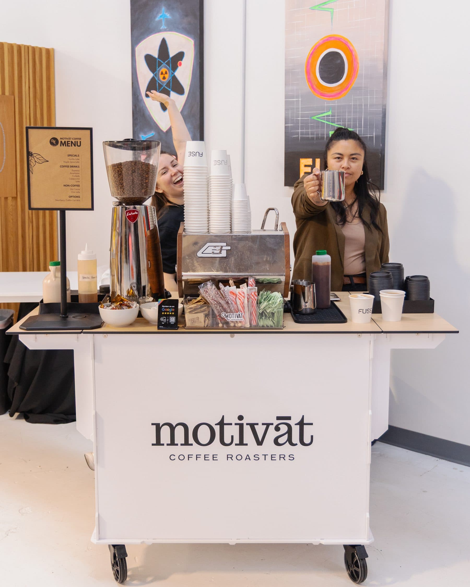 Motivāt baristas serving from the branded espresso cart at a corporate event